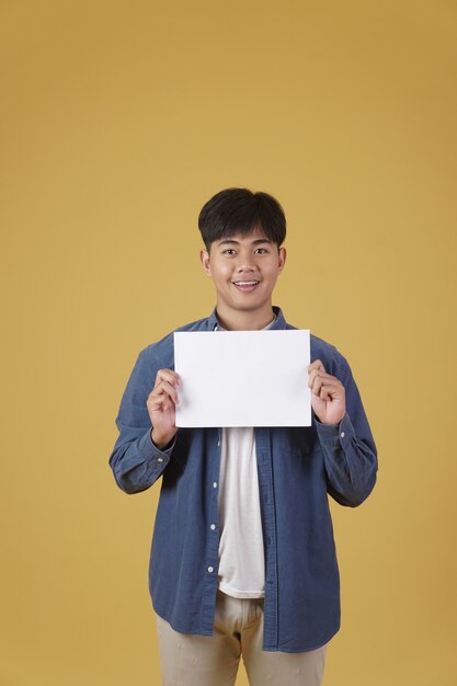 Portrait of smiling happy cheerful young asian man dressed casually showing blank empty placard paper isolated.