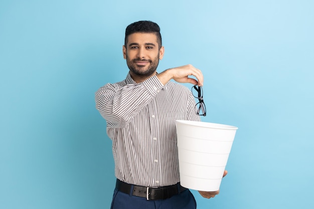 Portrait of smiling happy satisfied businessman throwing out\
his optical glasses after vision treatment looking at camera\
wearing striped shirt indoor studio shot isolated on blue\
background