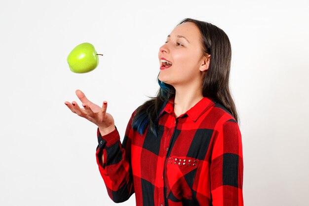 Portrait of a smiling happy woman throwing apple in the air on white wall