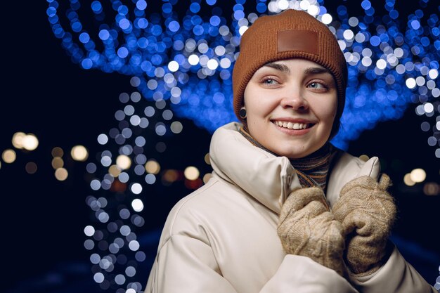 光る花輪と街の通りに立っている暖かい服装で笑顔の幸せな女性の肖像画