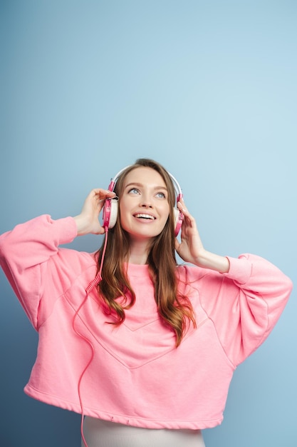 Portrait of smiling happy young woman wearing pink sweatshirt listening to music in headphones