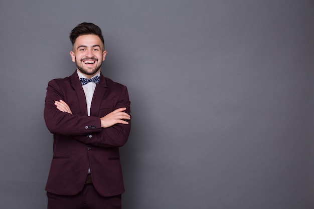 Portrait of smiling hipster man with hisarms crossed. Bearded man in dark red business suit standing