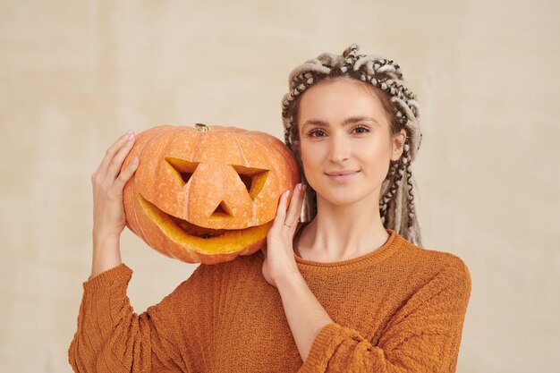 Photo portrait of smiling hipster young woman with white dreads posing with jackolantern on shoulder again