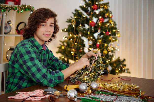 Portrait of smiling Hispanic teenage boy making Christmas decorations out of tinsel and candy canes