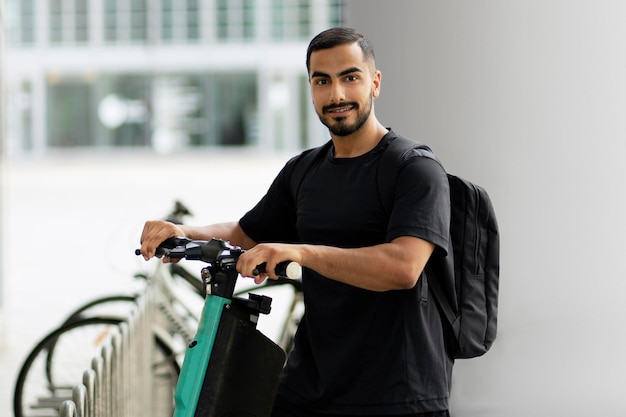 Portrait of smiling iranian man standing on electric scooter while preparing to the ride