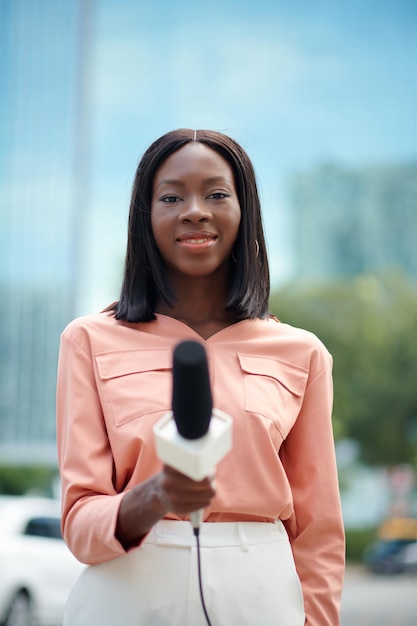 Portrait of smiling journalist with microphone standing outdoors