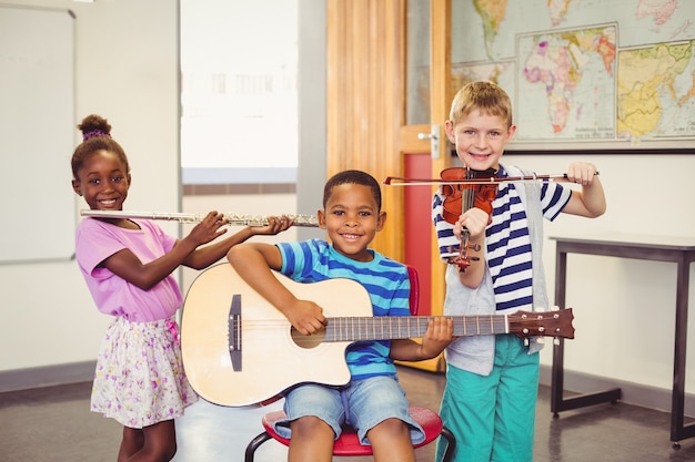 Portrait of smiling kids playing guitar, violin, flute in classroom