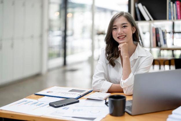 近代的なオフィスの職場でラップトップに取り組んでいる笑顔の女性起業家の肖像画