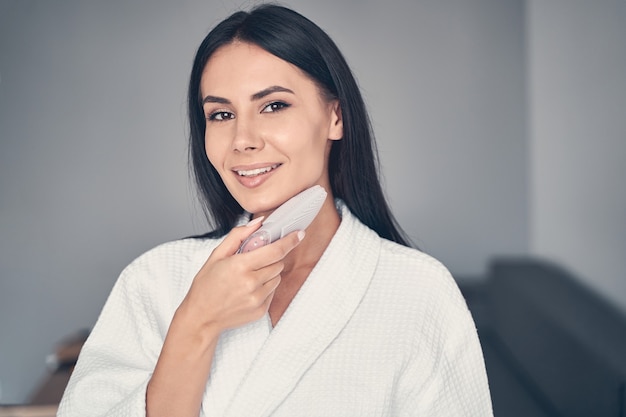 Portrait of a smiling lady with a silicone face cleansing brush posing for the front