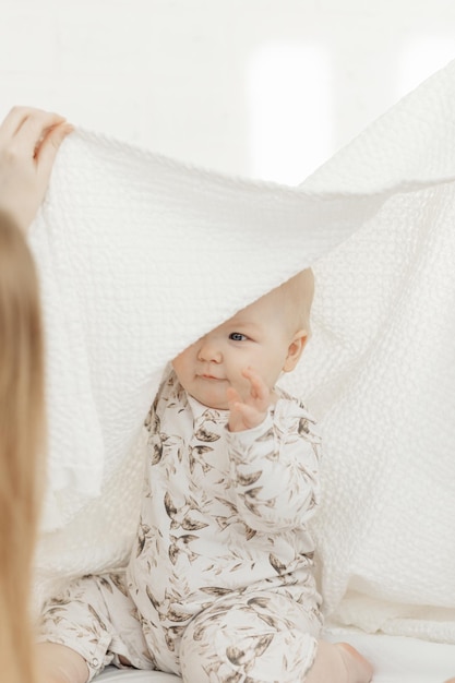 Photo portrait of smiling little blueeyed plump baby infant toddler covered with cotton blanket sitting on