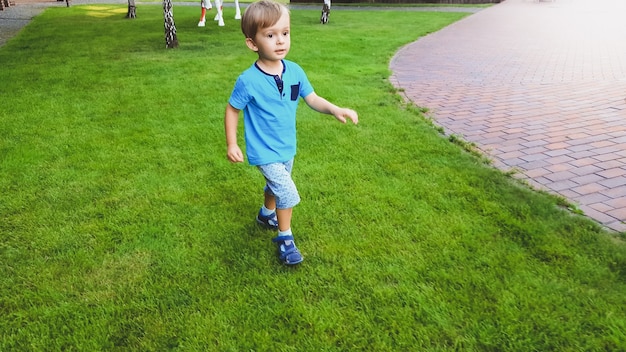 Portrait of smiling little boy running on grass lawn at park