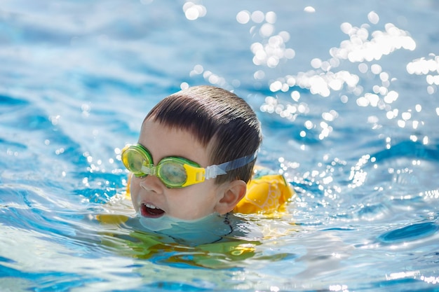 portrait of smiling little boy swims in the pool in inflatable vest and goggles