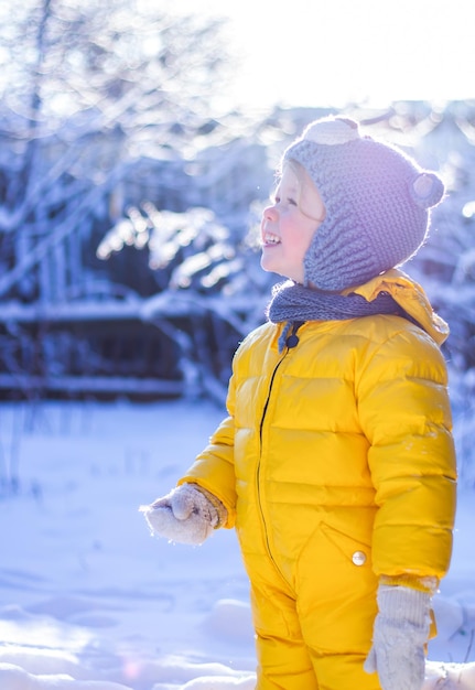 Portrait of smiling little child girl in blue hat and yellow snowsuit on sunny winter day