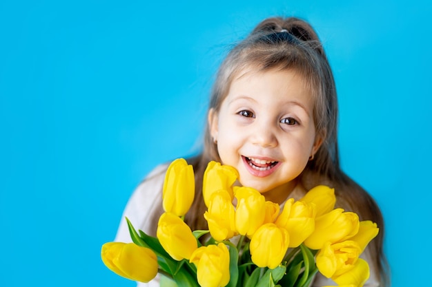 Portrait of a smiling little girl a child with a bouquet of yellow tulips on a blue isolated background Lifestyle International Women's or Mother's Day Space for text Highquality photography