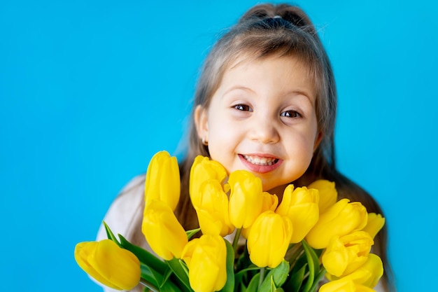 Ritratto di una bambina sorridente un bambino con un mazzo di tulipani gialli su sfondo blu isolato stile di vita giornata internazionale della donna o della mamma spazio per il testo fotografia di alta qualità