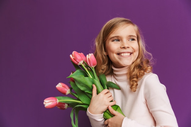 Портрет улыбающейся маленькой девочки, держащей букет тюльпанов на фиолетовой стене