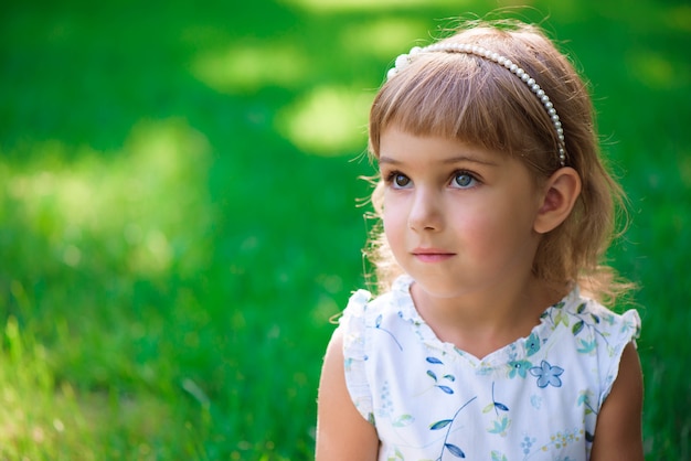 Portrait of a smiling little girl with heterochromia two colored eyes sitting on green grass.
