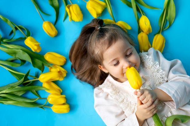 Portrait of a smiling little girl among yellow tulips on a blue monochrome background Lifestyle Fresh flowers International Women's Day or Mother's Day Space for text Highquality photography