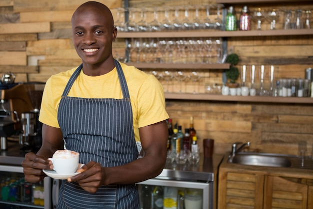 カフェでコーヒーカップを保持している笑顔の男性バリスタの肖像画