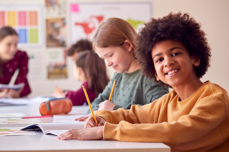 Photo portrait of smiling male elementary school student working at desk in classroom with teacher
