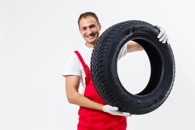 白い背景の上のタイヤを保持している笑顔の男性のメカニックの肖像画