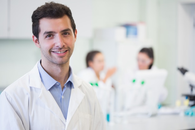 Portrait of a smiling male researcher with colleagues in the background at laboratory