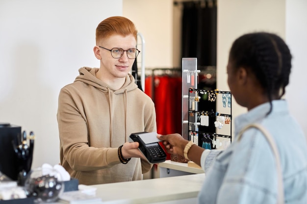 Portrait of smiling male store manager processing credit card payment from female customer