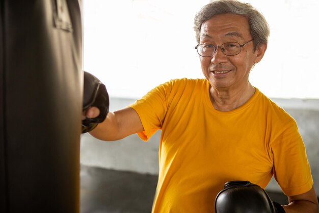 Photo portrait of smiling man exercising with punching bag in gym