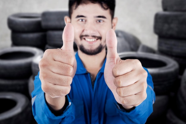 Foto ritratto di un uomo sorridente che fa un gesto mentre è in piedi vicino a una pila di pneumatici