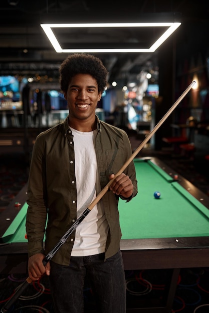 Portrait of smiling man holding billiards cue stick with pool table on background