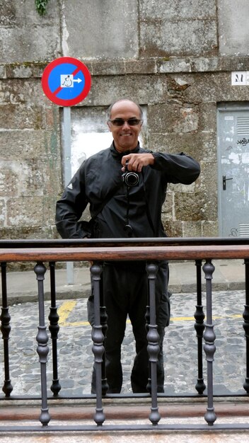 Portrait of smiling man holding camera against building