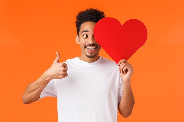 Portrait of smiling man holding heart shape against orange background