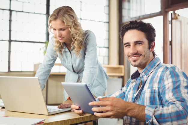 Portrait of smiling  man holding tablet with woman working in office 