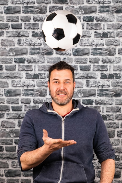 Foto ritratto di un uomo sorridente che gioca con una palla da calcio contro un muro di mattoni