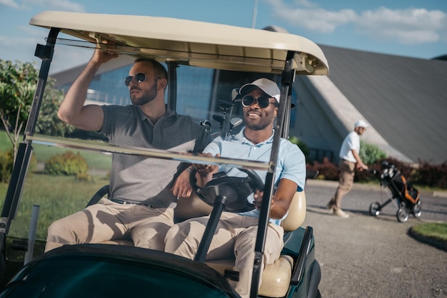 Portrait of smiling man riding golf cart with friend sitting near by