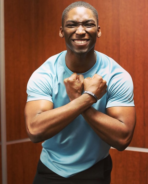 Portrait of smiling man showing muscles while standing against wall