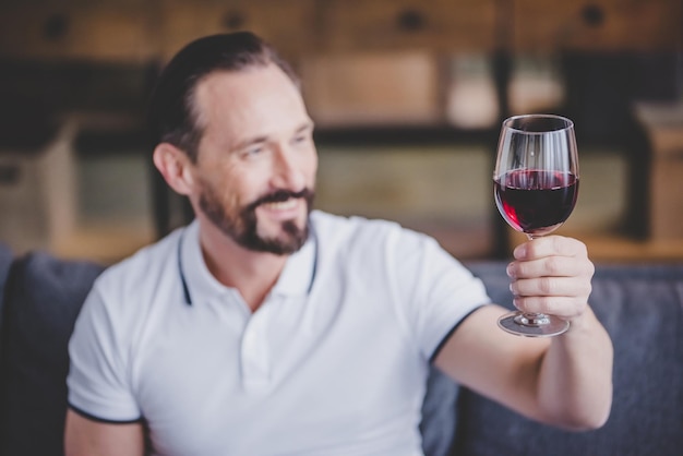 Портрет улыбающегося мужчины, сидящего на диване и держащего бокал красного вина