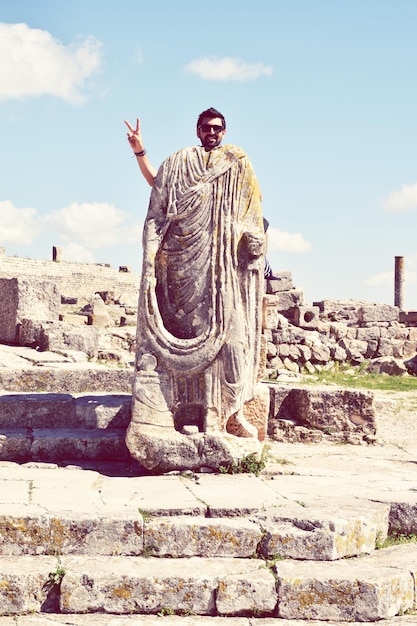 Foto ritratto di un uomo sorridente in piedi dietro una scultura rotta contro il cielo in un luogo storico