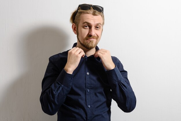 Portrait of smiling man in sunglasses standing near a wall and holding hands on the shirt collar