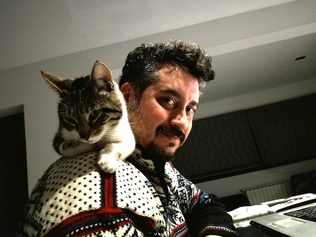 Foto ritratto di un uomo sorridente con un gatto sulle spalle a casa