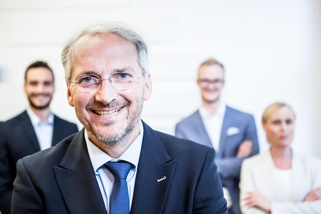 Photo portrait of smiling mature businessman with colleagues standing in office