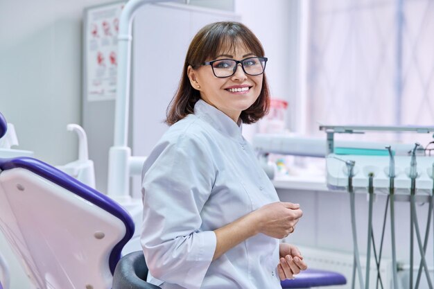 Портрет улыбающейся зрелой женщины-стоматолога, смотрящей в камеру в офисе Позитивный врач средних лет в очках Стоматология, медицина, профессия, концепция лечения, стоматология