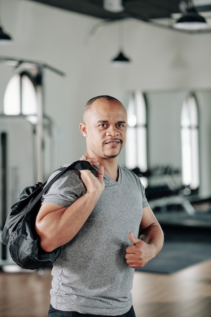 Portrait of smiling mature fit man standing with gym bag and showing thumbs-up