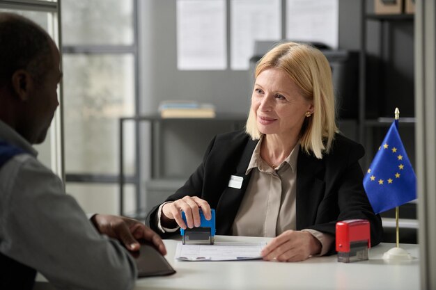 Portrait of smiling mature woman consulting person in eu immigration office or government agency and