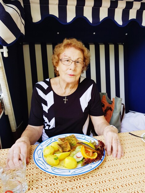 Портрет улыбающейся взрослой женщины с тарелкой с едой на столе