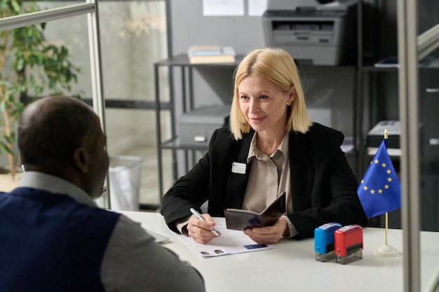 Portrait of smiling mature woman working in immigration office and consulting african american clien