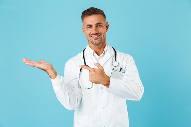 Портрет улыбающегося врача со стетоскопом, стоящего изолированно над синей стеной