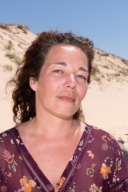 Portrait smiling middle aged brunette curly woman at the beach and blue sky