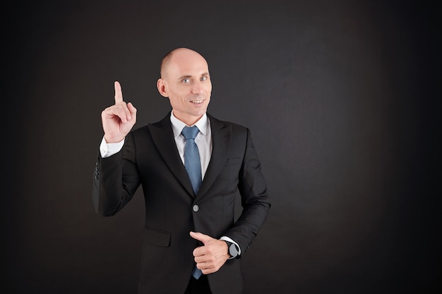 Portrait of smiling middle-aged businessman raising index finger as he is having new creative idea