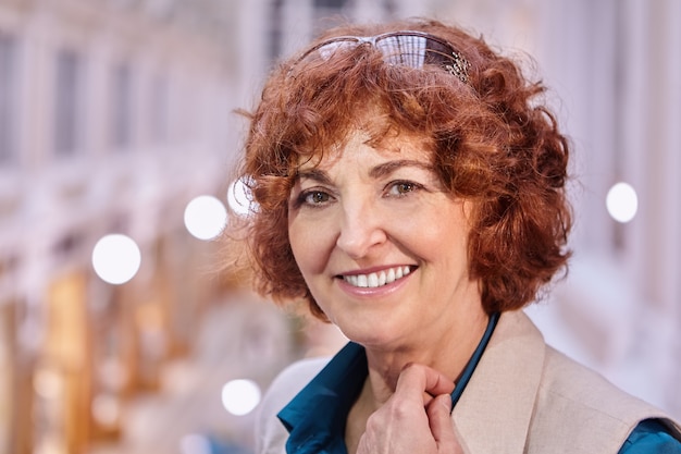 Portrait of smiling middle-aged caucasian woman with red short curly hair and sunglasses.